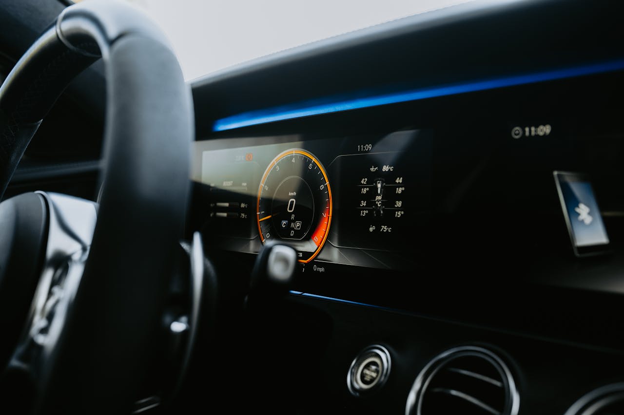 services-03 Close-up view of a sleek car dashboard featuring an illuminated digital display and steering wheel.